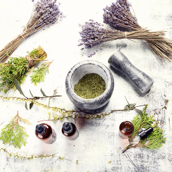 A marble mortar and pestle surrounded by dried lavender, herbs, and essential oil bottles.