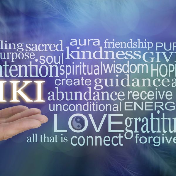 Hand offering glowing Reiki word with spiritual and healing terms around it.