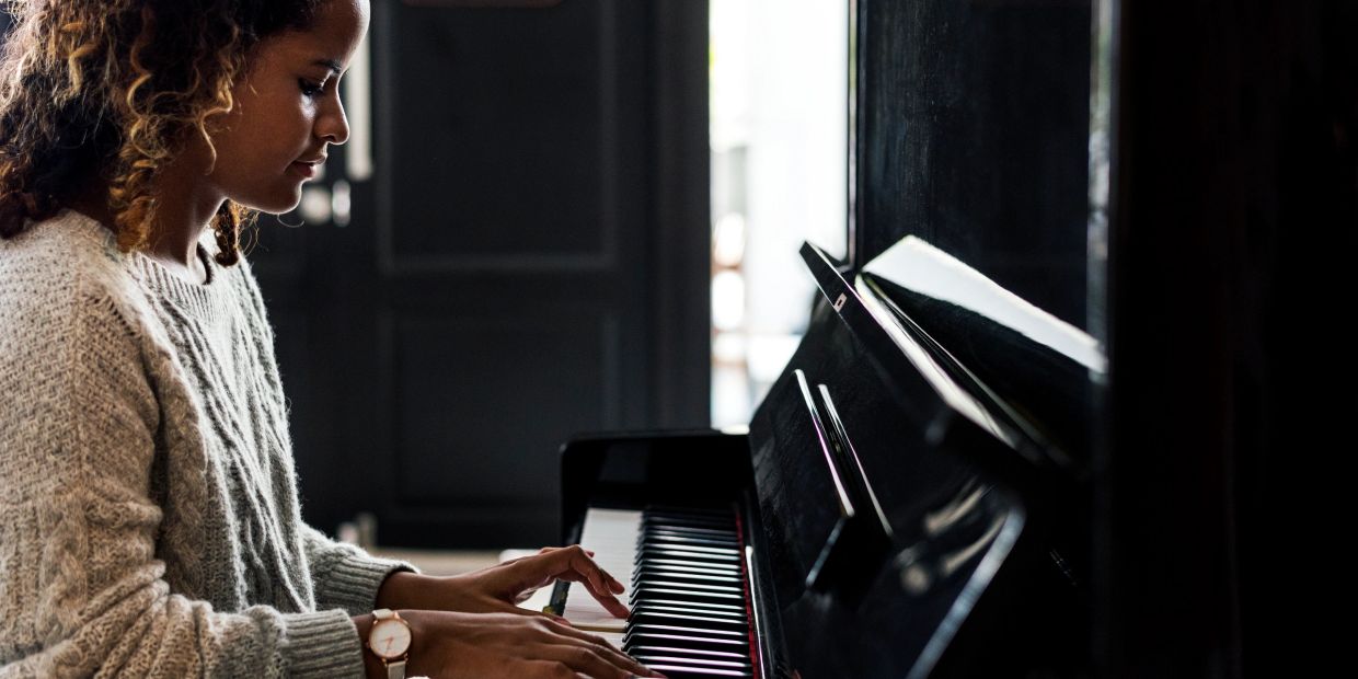 A woman playing the piano indoors, focused and serene.