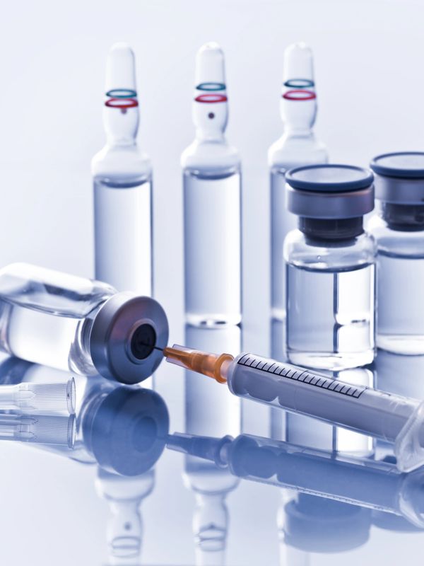 Syringe drawing liquid from a vial with ampoules in the background.
