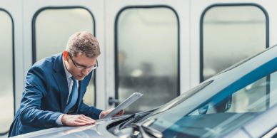 A man inspecting a car with documents.