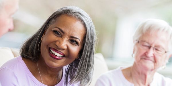 Two elderly women smiling and chatting together indoors.