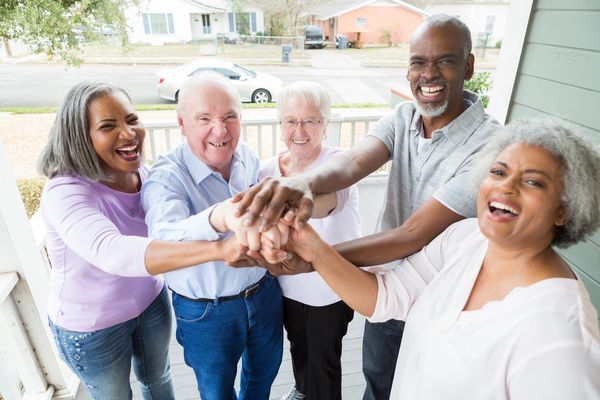 Group of diverse seniors joining hands and smiling.