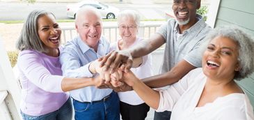 Happy diverse seniors joining hands in a group on a porch.