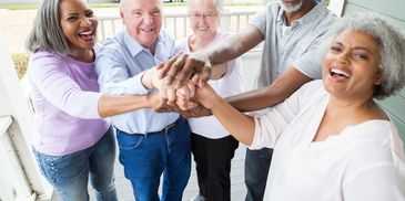 Happy diverse seniors joining hands in a group on a porch.