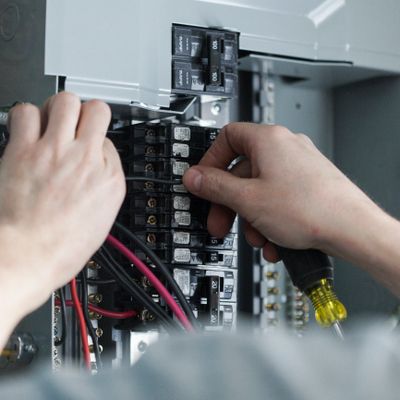 Hands working on an electrical circuit breaker panel.