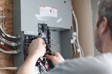 Electrician working on an electrical panel with tools in hand.