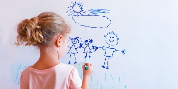 A young girl drawing a happy family on a white wall.