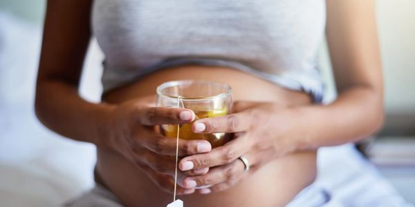 Pregnant woman holding a cup of tea, resting hands on belly.