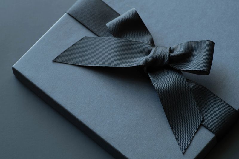 Black gift box on a dark contrasted background, decorated with a textured bow and feathers, creating a romantic atmosphere. Typically used for birthday, anniversary presents, gift cards, post cards, letters.