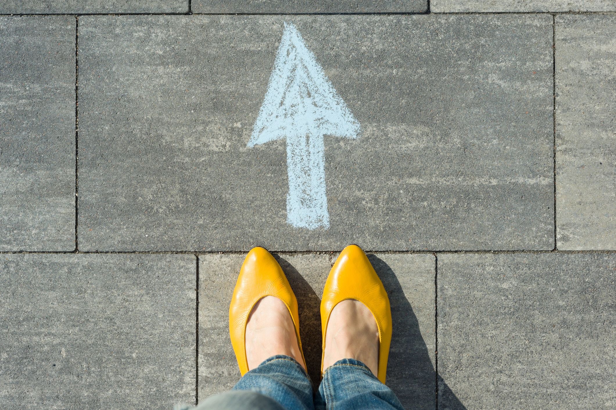 Woman standing on a pavement behind a blue arrow written onto pavement in chalk indicating the next 