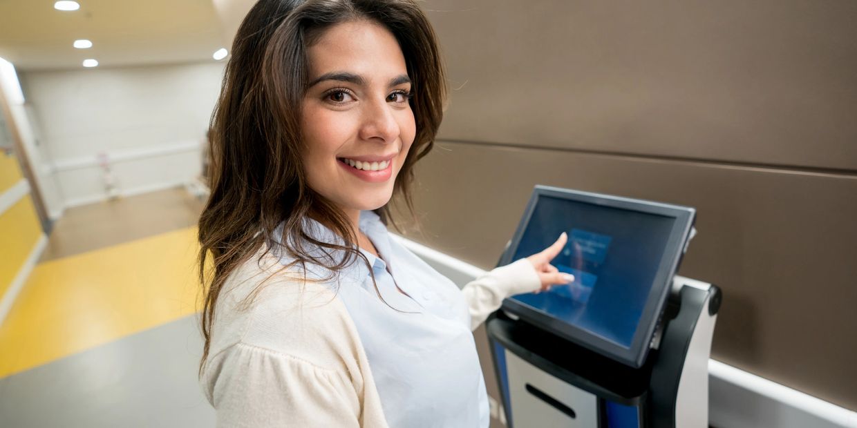 Smiling woman using a touchscreen kiosk in a modern indoor setting.