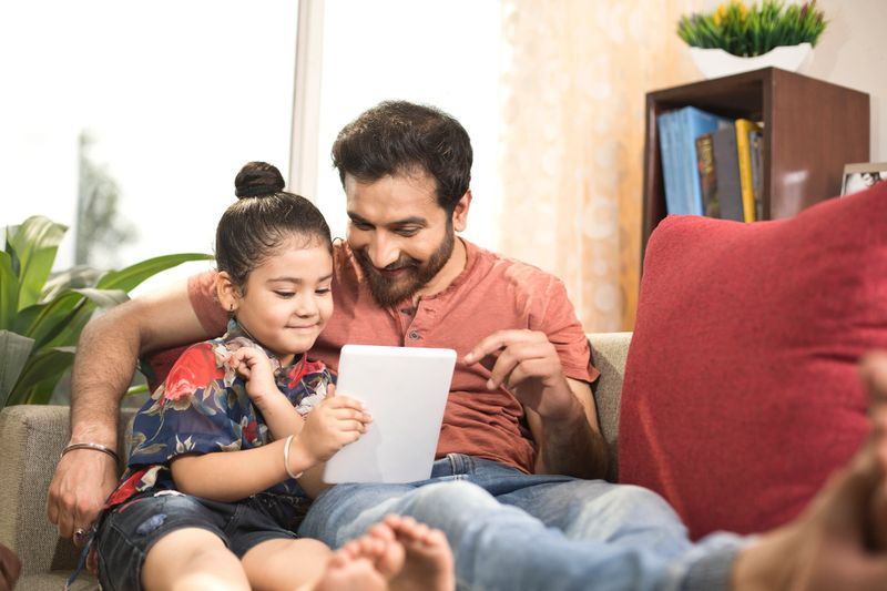 Father with little daughter using digital tablet at home