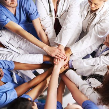 Healthcare professionals unite hands in a team huddle, symbolizing teamwork and support.