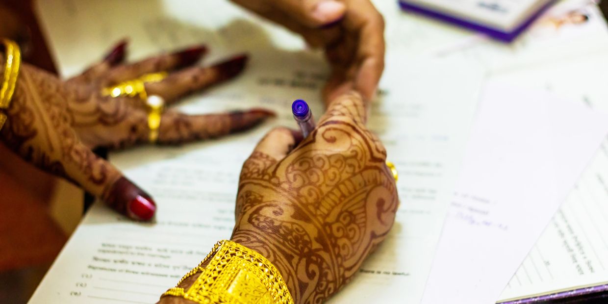 Henna-decorated hands with gold jewelry writing on paper.