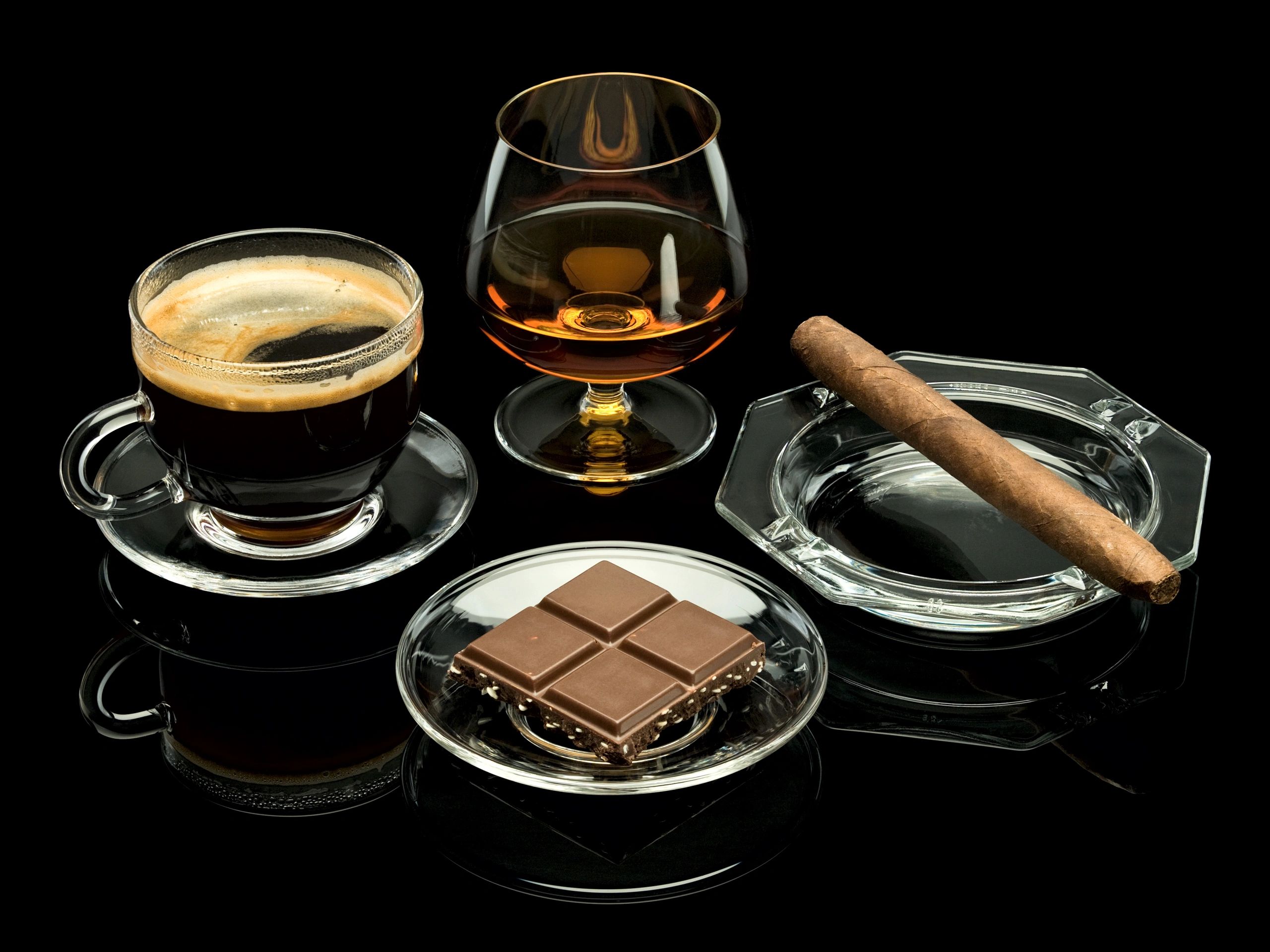 Coffee, cognac, chocolate, and a boutique cigar on glassware against black.