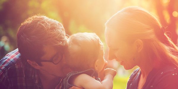 Parents lovingly interacting with their baby outdoors in warm sunlight.