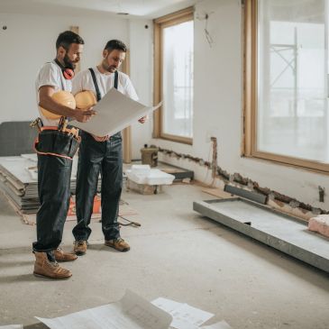 Two construction workers reviewing blueprints onsite.