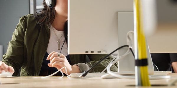 Woman wearing headphones working on a computer in an office.