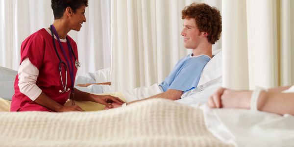 Nurse talking with a young male patient in hospital bed, showing care and support.
