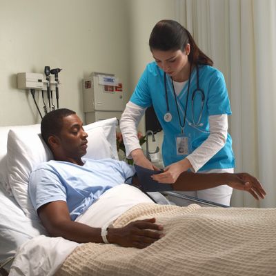 Nurse checking blood pressure of a male patient in hospital bed.