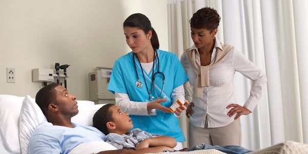 Nurse explaining medication to a patient and family in a hospital room.
