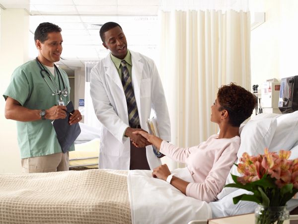 Doctor shakes hands with patient in hospital bed while nurse observes.