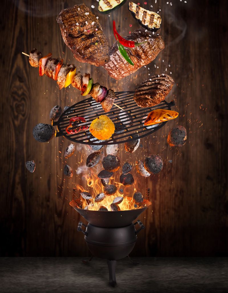 Kettle grill with hot briquettes, cast iron grate and tasty beef steaks flying in the air. Freeze motion barbecue concept.