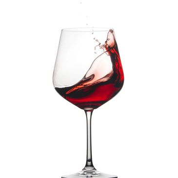 Red wine splashing inside a clear wine glass against a white background.