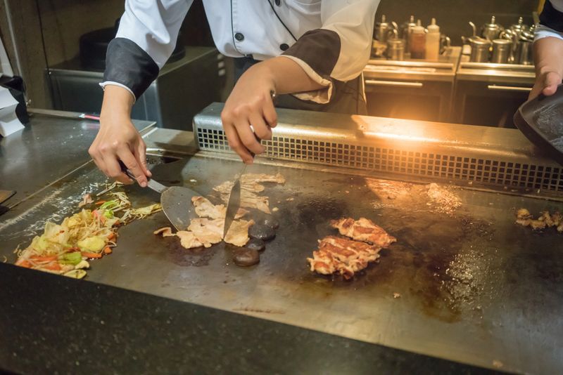 Hand of Chef cooking beef steak on hot pan in front of customers. Tepanyaki steak