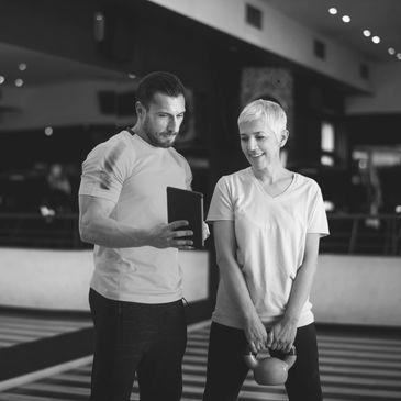 A trainer guiding a woman lifting a kettlebell in a gym.