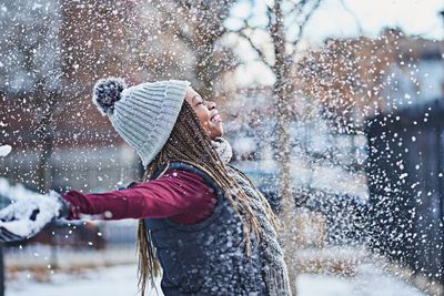 POC smiles with her arms wide open smiling as the snow falls in winter scene.