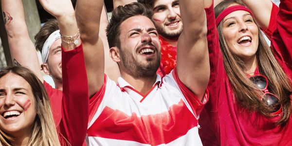 Excited sports fans cheering enthusiastically in red and white attire.