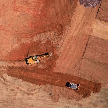 Aerial view of excavators working on red soil at a construction site.
