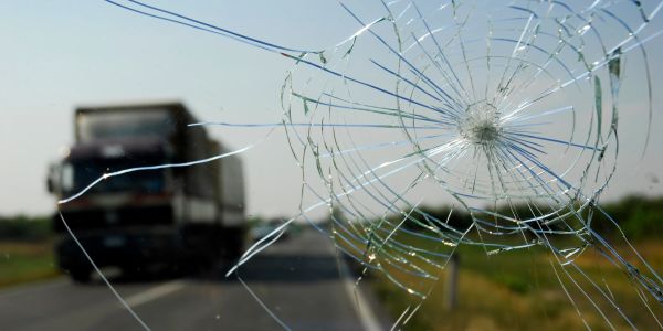 Cracked windshield with blurred truck in background.