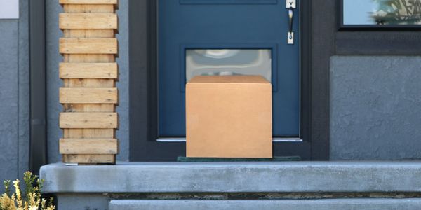 A cardboard package sits on a doorstep with a blue door in the background.