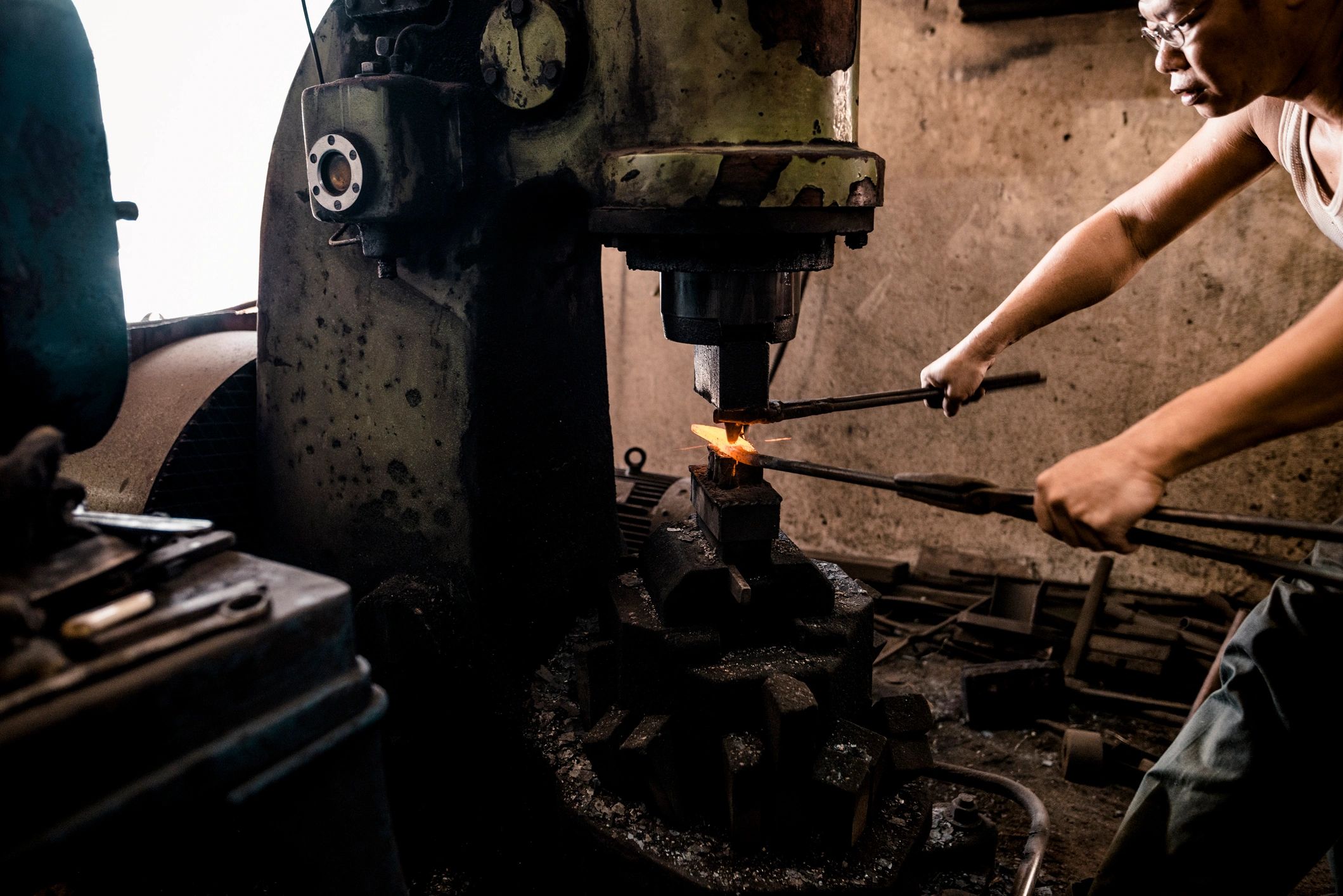 Blacksmith forging hot metal with machine press.