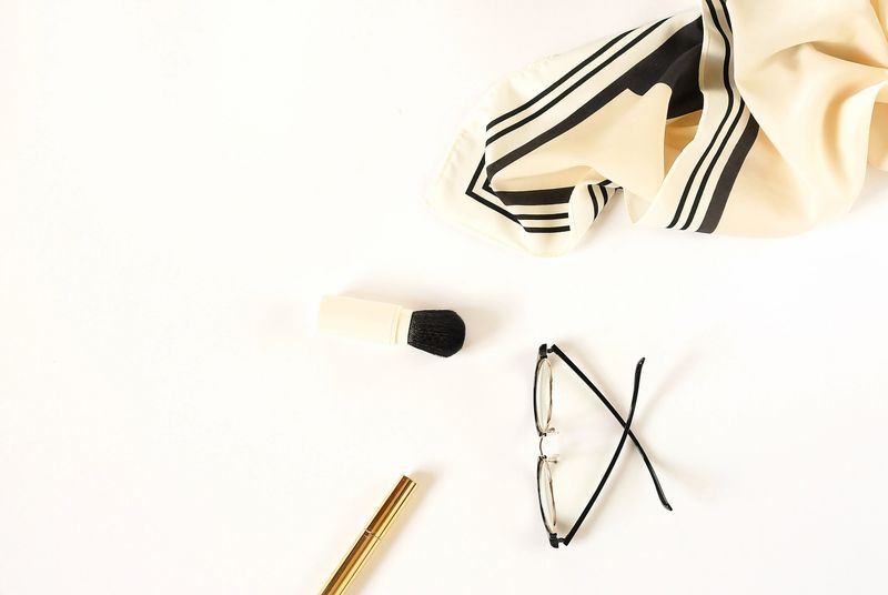 Pretty women's accessories bag, silk handkerchief, glasses, watch, bracelet and cosmetics in gently pastel beige tones on a white background.