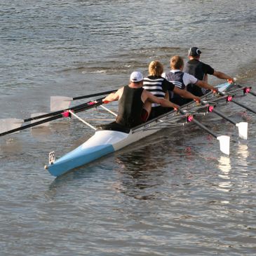 Four people rowing a boat on water.