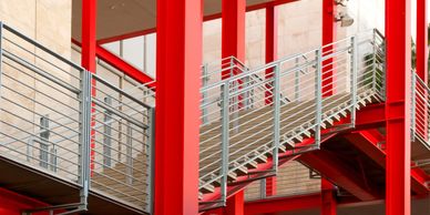 Modern staircase with red beams and metal railings in a building.