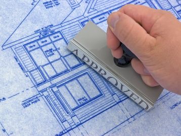 Hand stamping an 'APPROVED' mark on a building blueprint.