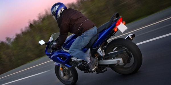 Motorcyclist in helmet riding a blue sportbike at dusk on the road.