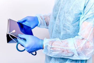 Healthcare professional using a tablet while wearing gloves and protective gown.
