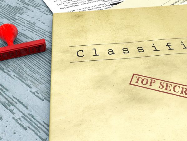 A top secret stamp and classified folder on a table.