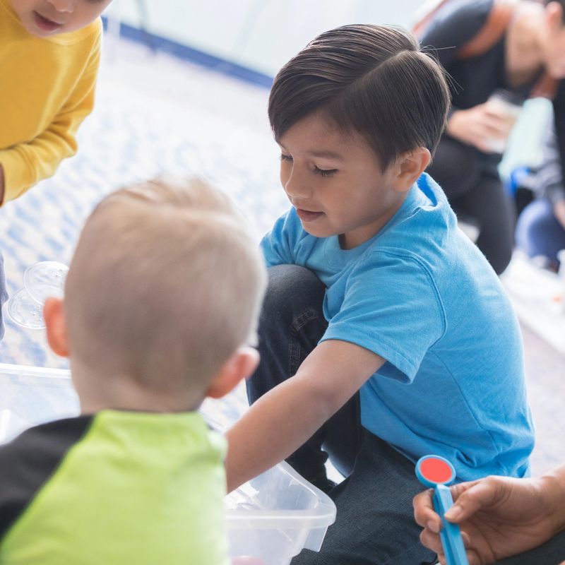 Adorable preschool students play in a sensory bin. They are enjoying exploring the items in the sensory bin.