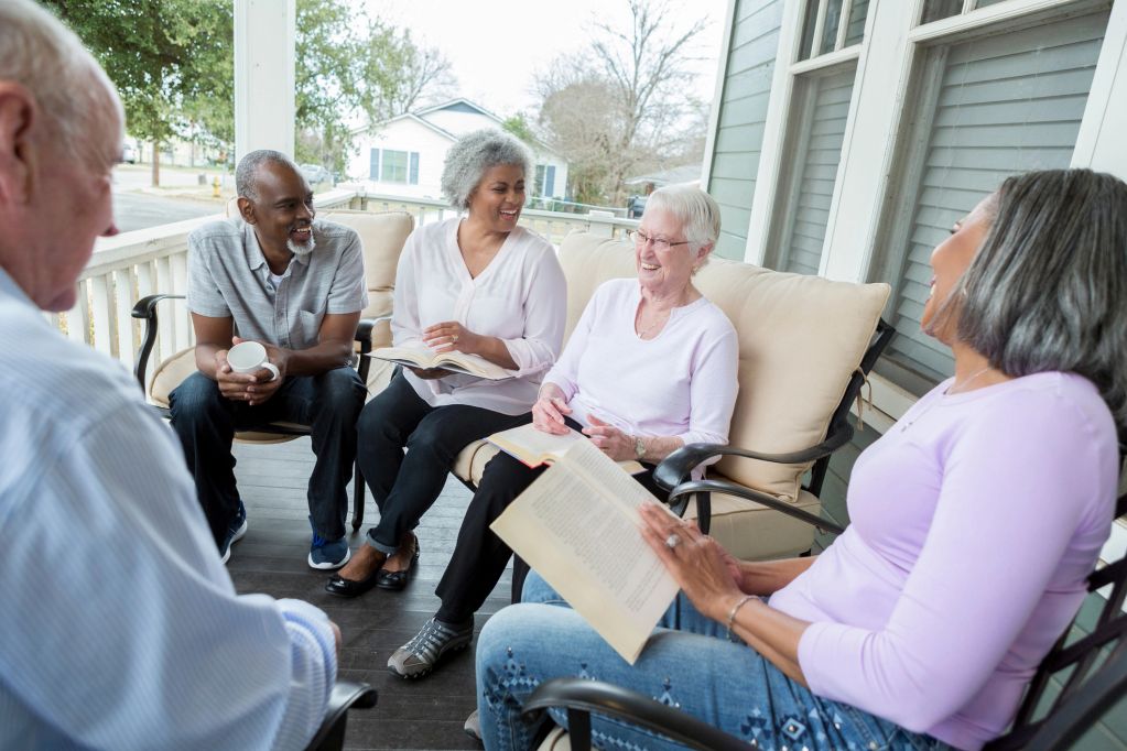 Group of older adults reading and chatting on a porch.