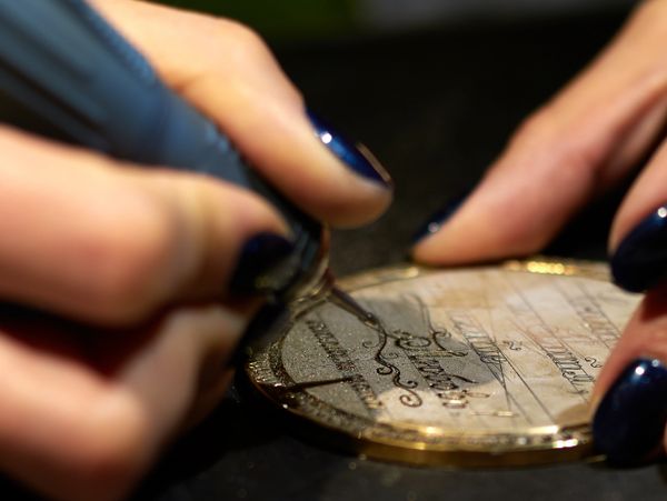 Close-up of hands engraving intricate designs on a metallic surface.