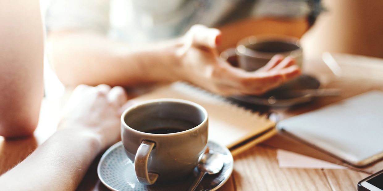 Two people having coffee and conversation at a wooden table.