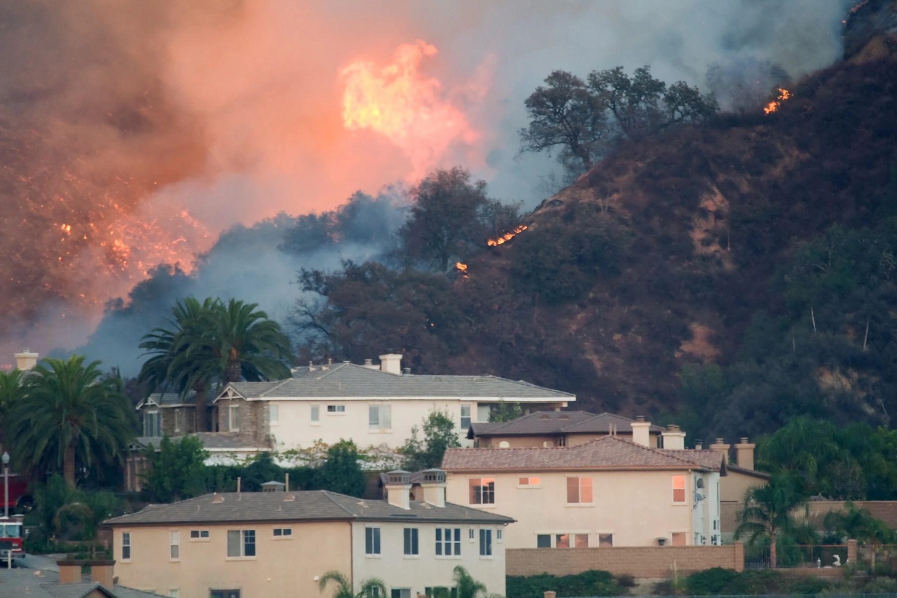 Wildfire burning on hillside near houses.