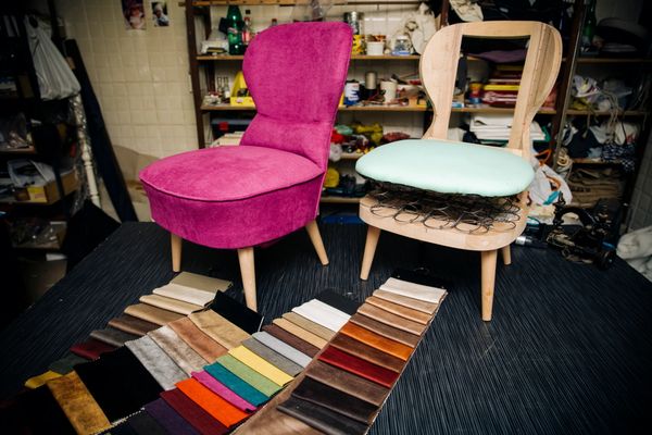 A vibrant pink upholstered chair next to an unfinished chair with fabric swatches.